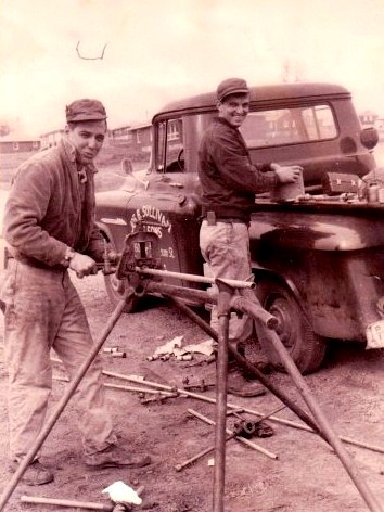 Two Sullivan plumbers threading pipe at their service truck, mid-1900s